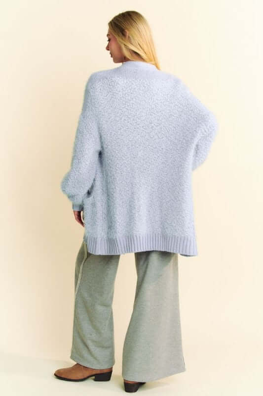 Woman in a cozy light blue cardigan with long sleeves and ribbed hem, paired with gray pants from the back.