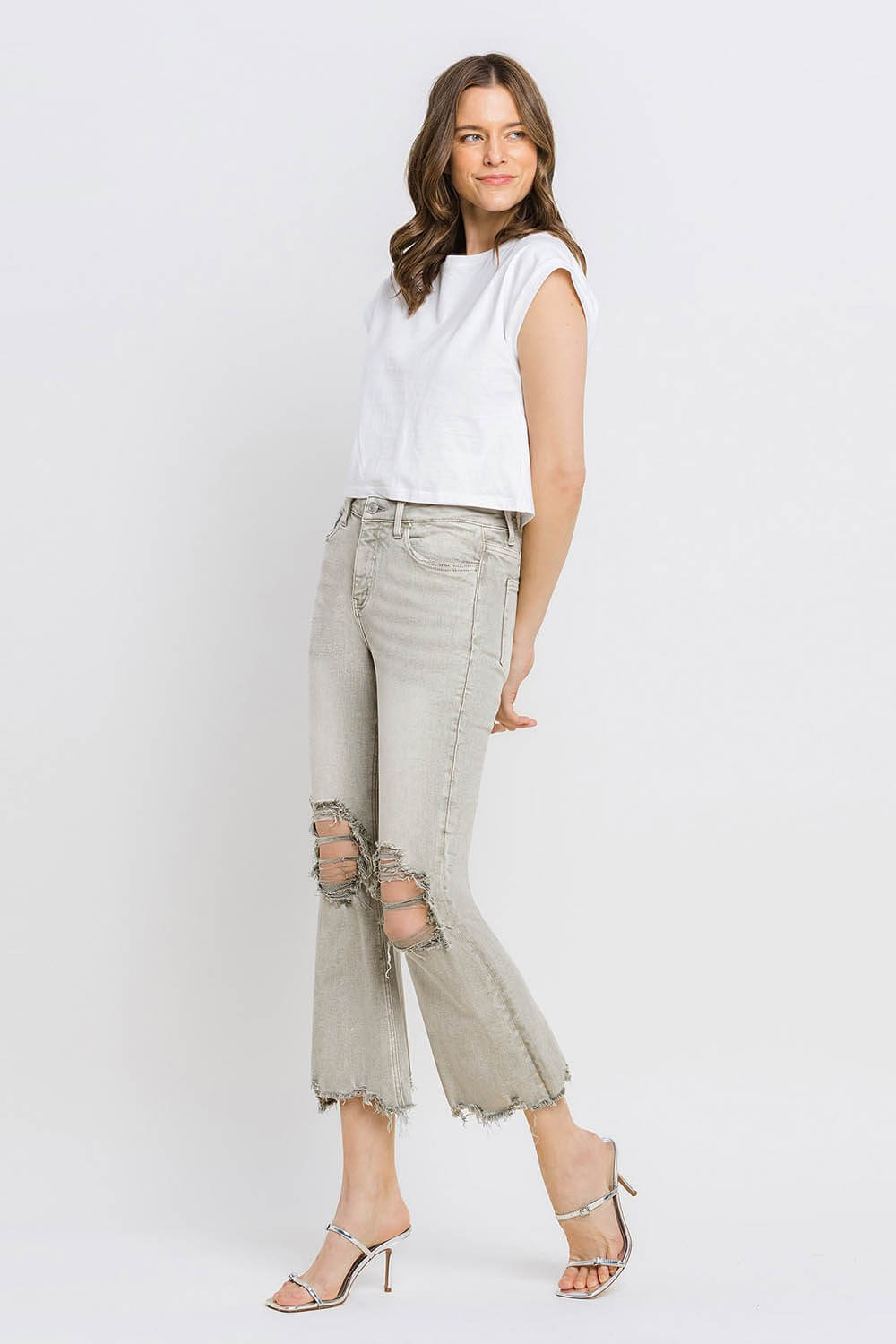 Woman wearing Lovervet distressed raw hem cropped flare jeans with a white top and heels.