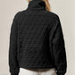 Woman wearing black quilted half zip sweatshirt with pocket, styled with white shorts, showcasing cozy yet stylish fashion.