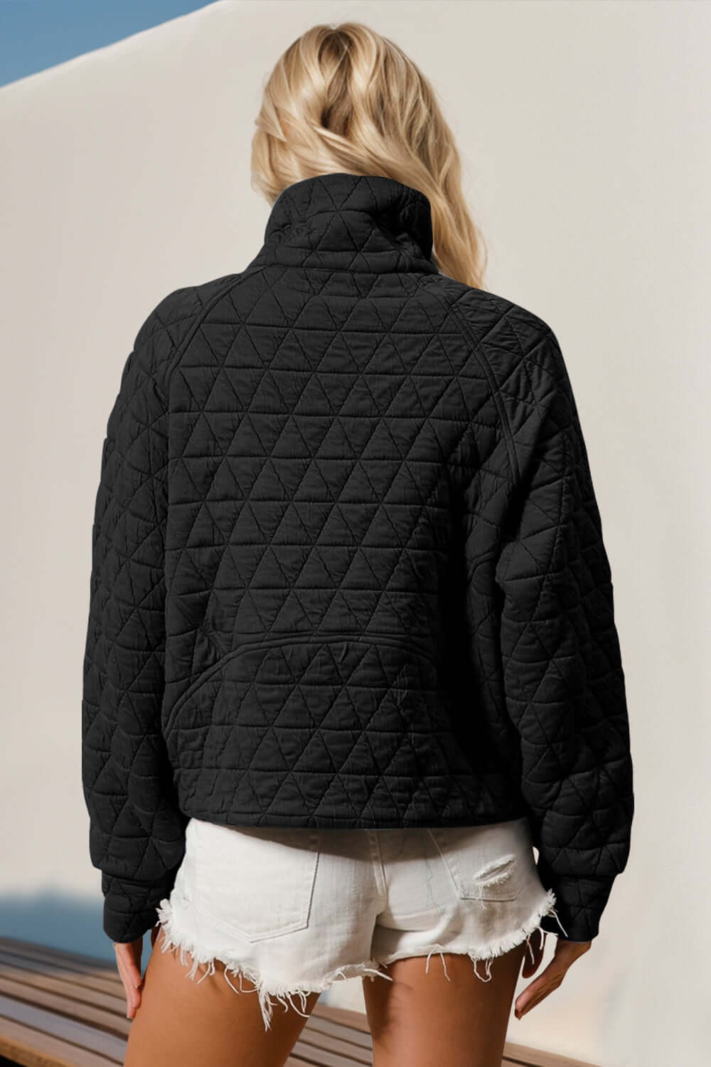 Woman wearing black quilted half zip sweatshirt with pocket, styled with white shorts, showcasing cozy yet stylish fashion.