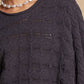 Dark gray cable knit cropped sweater with round neck and unique texture, worn with a pearl necklace, for a cozy and chic look.