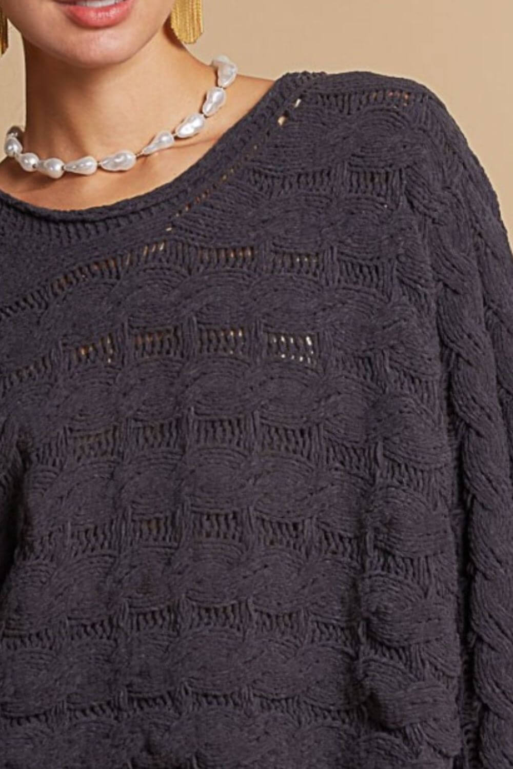 Dark gray cable knit cropped sweater with round neck and unique texture, worn with a pearl necklace, for a cozy and chic look.