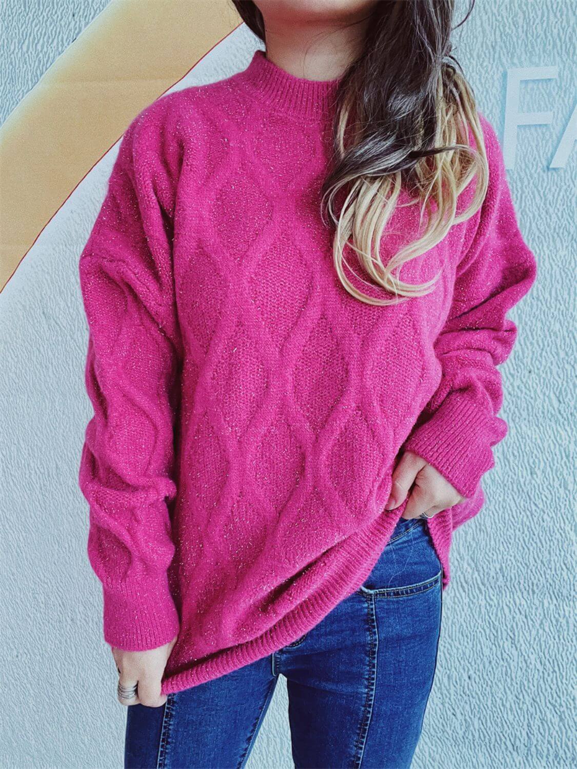 Woman wearing Bella Road Diamond Round Neck Long Sleeve Sweater in vibrant pink with a diamond pattern, paired with blue jeans.