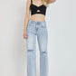 Woman wearing high rise distressed wide leg Risen Jeans with a black cropped top and sandals, showcasing trendy and edgy denim fashion.