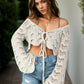 Young woman in cream openwork flare sleeve cover-up paired with denim shorts, exuding a stylish beach vibe.