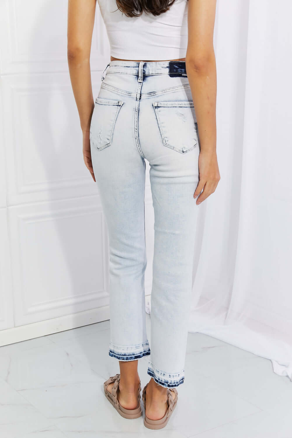 Woman wearing Camille Acid Wash Crop Straight Jeans by Risen Jeans, showcasing the back view with slight distressing and trendy cropped length