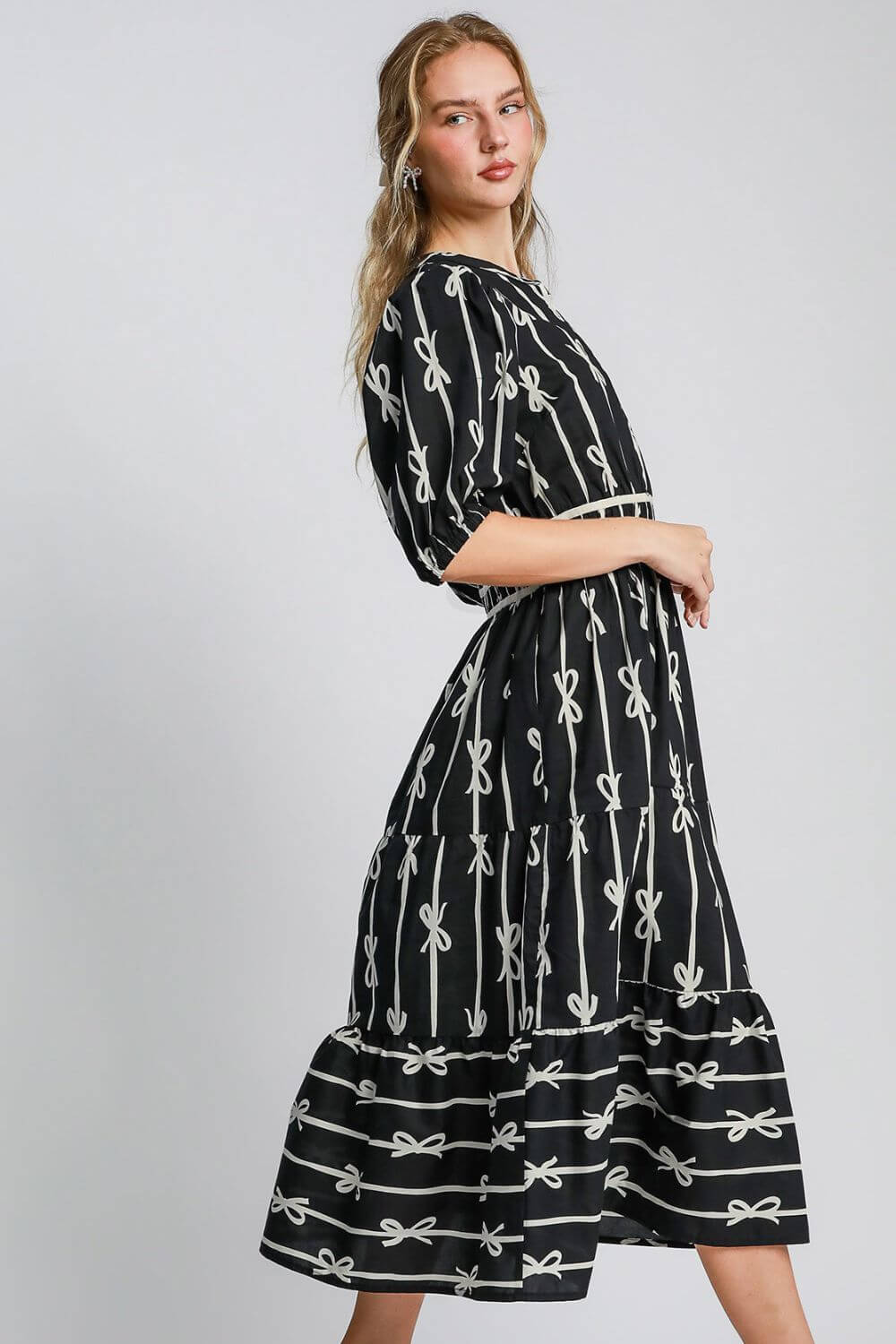 Model showcases elegant Umgee midi dress with whimsical bow tie print and luxurious velvet trim, perfect for special occasions.