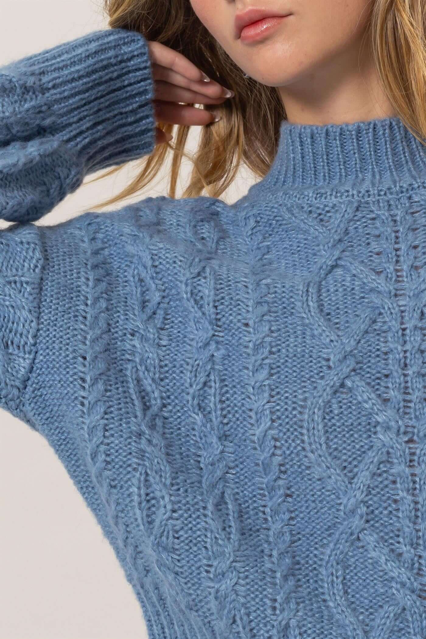 Close-up of a cozy blue cable-knit mock neck sweater with dropped shoulders, showcasing its stylish texture and relaxed fit.