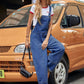 Woman wearing Bella Road Wide Strap Denim Overalls leans against a vintage taxi, showcasing stylish wide leg design.