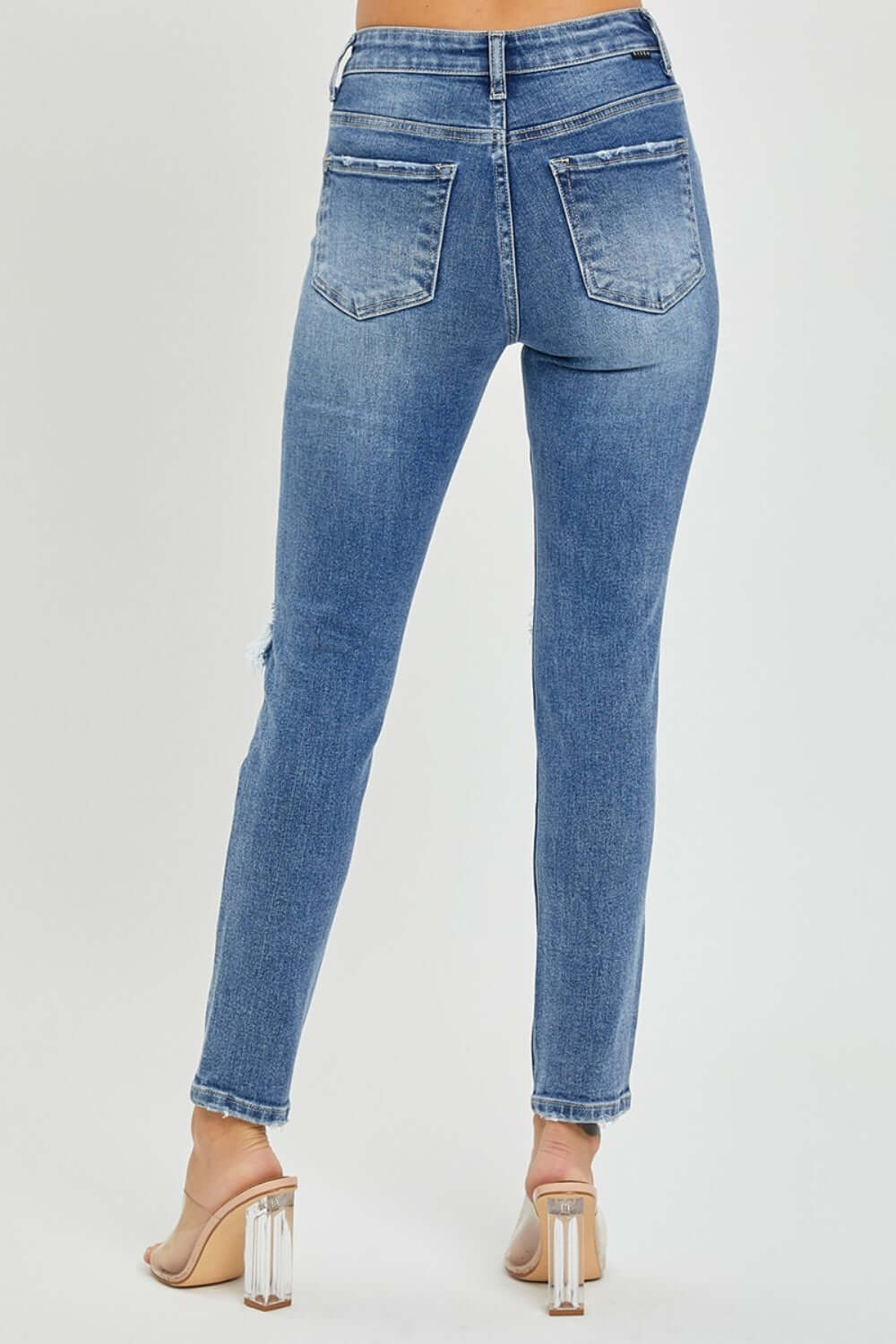 Woman modeling Risen Jeans High Rise Knee Distressed Skinny Jeans back view showing pockets and hem details.