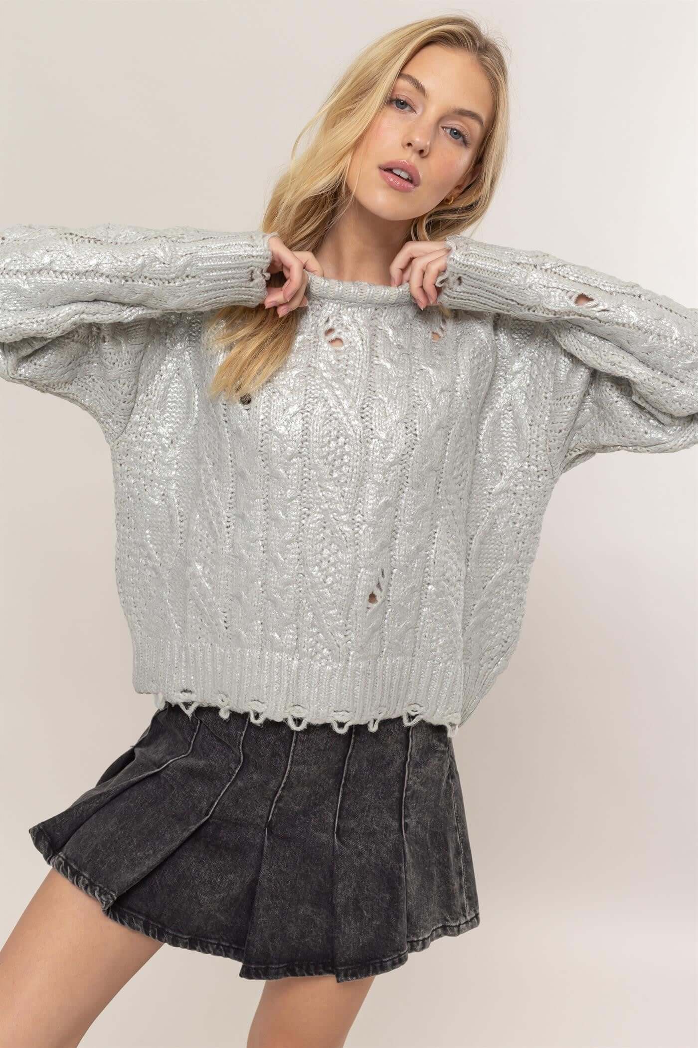 Fashion model wearing distressed cable-knit round neck long sleeve sweater, styled with a denim skirt for a chic casual look.