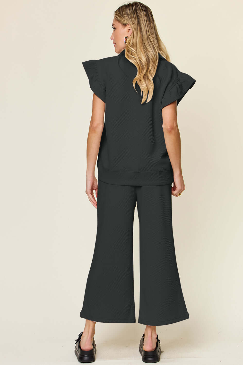 Back view of woman wearing Texture Ruffle Short Sleeve Top and Drawstring Wide Leg Pants Set in black.