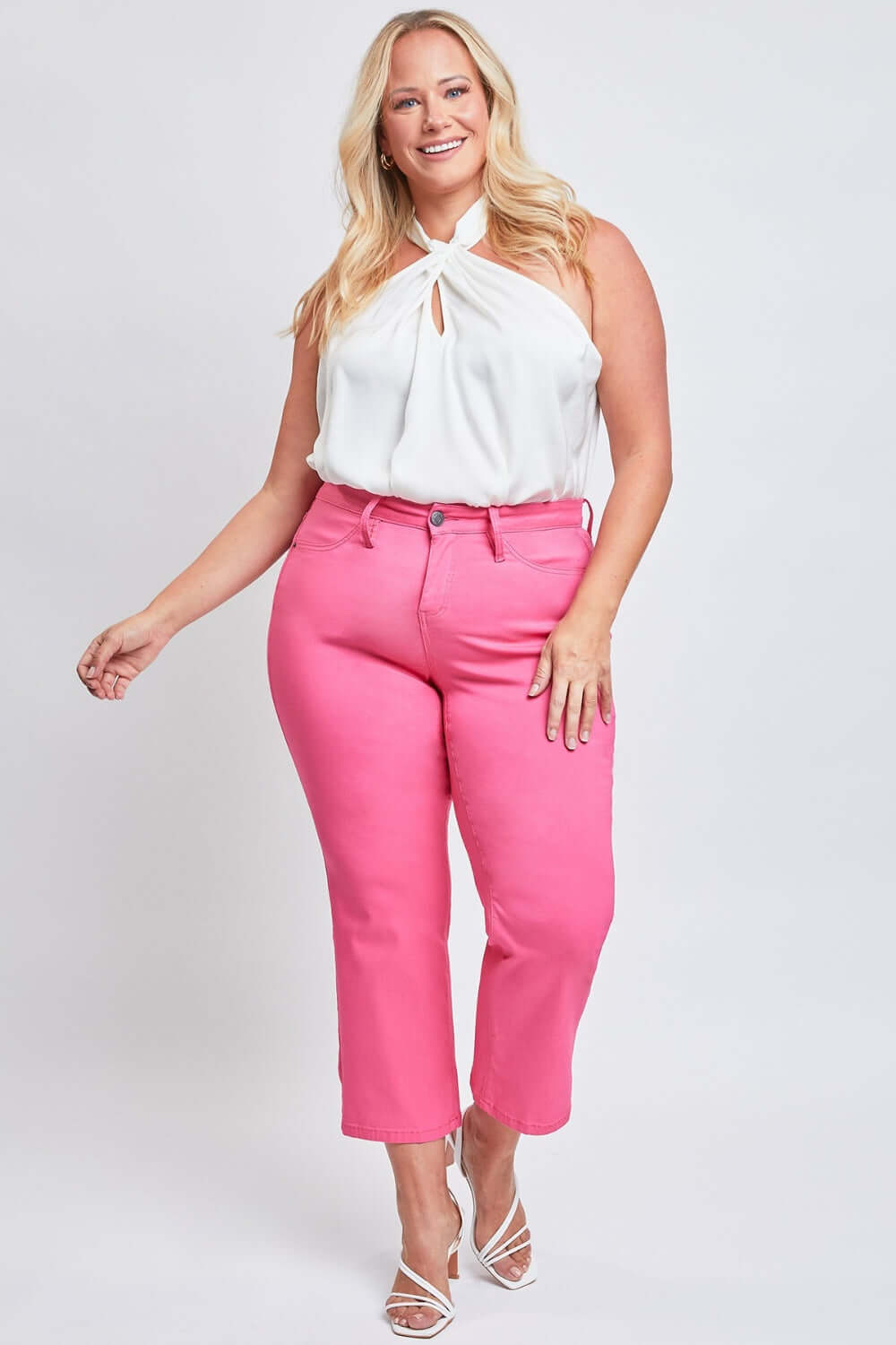 Smiling woman wearing a white halter top and pink Mid-Rise Hyperstretch Cropped Straight Pants from YMI Jeans.