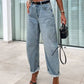 Woman wearing high waist wide leg jeans with a black crop top and heels, holding a black handbag in an indoor setting.