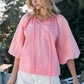 Woman wearing pink Poplin Bubble Sleeve Blouse and hat, paired with white shorts, outdoors.