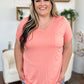 Woman wearing Basic Bae Bamboo Full Size V-Neck Short Sleeve T-Shirt in pink, smiling in a cozy living room setting.