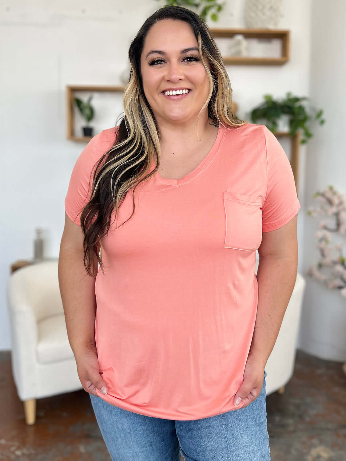 Woman wearing Basic Bae Bamboo Full Size V-Neck Short Sleeve T-Shirt in pink, smiling in a cozy living room setting.