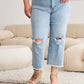 Woman wearing Tummy Control High Waist Raw Hem Distressed Jeans, RFM Jeans, in bright living room with sofa in the background.