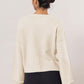 Back view of a woman in a cream dropped shoulder ribbed sweater paired with black leggings, showcasing a relaxed style.