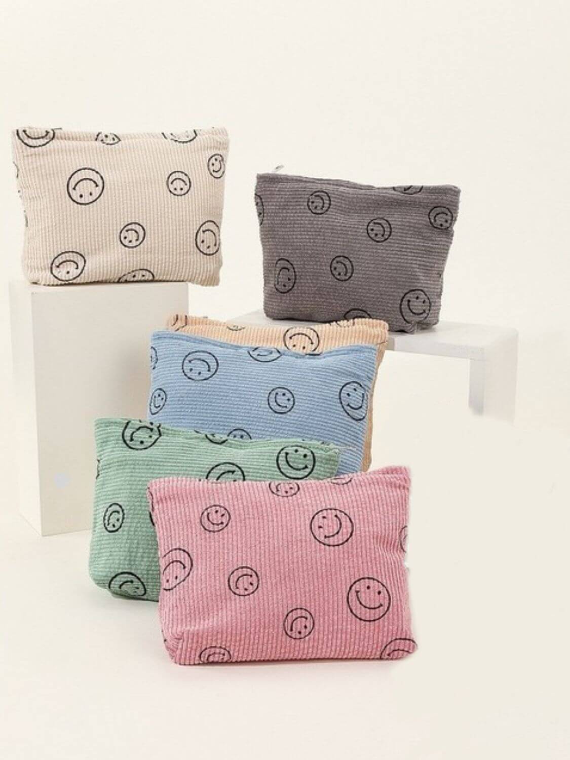 Five colorful corduroy clutch bags featuring playful smiley face prints, perfect for trendy casual outings.