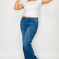 Woman in high-rise straight jeans and a white crop top, playfully adjusting her hat against a light background.