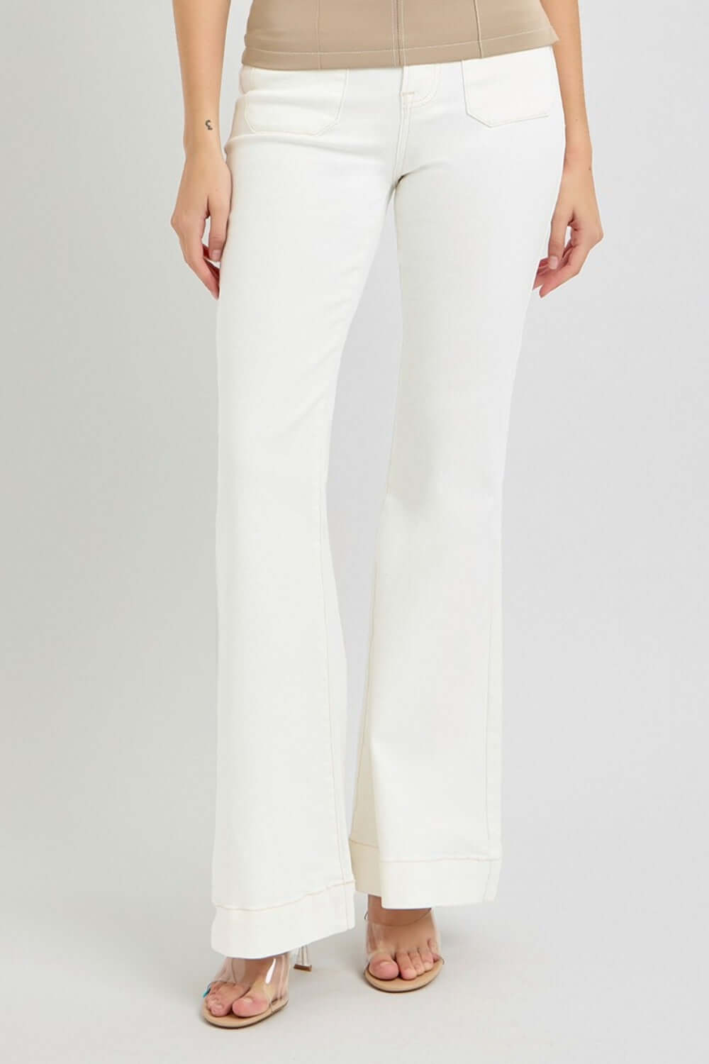 Woman wearing RISEN full size high rise flare jeans with front patch pockets in white, showcasing stylish and trendy look.