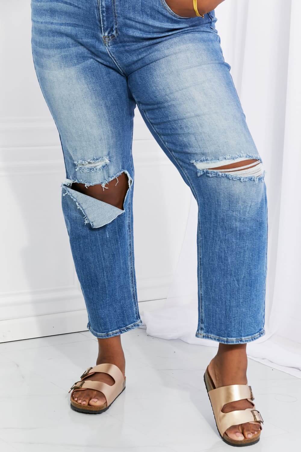 Emily High Rise Relaxed Jeans with ripped knee details, cropped length, styled casually with metallic sandals. Risen Jeans style.