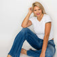 Woman in white t-shirt and distressed high rise jeans, sitting comfortably, showcasing stylish pockets and relaxed fit.