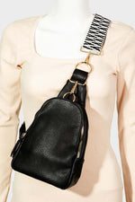 Chic black faux leather sling bag with a stylish patterned strap, perfect for everyday use and versatile outfit pairing.