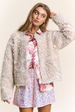 Fashionable woman in chic, textured J.NNA jacket with mixed fabrics, styled over a floral top and sparkly skirt.