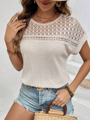 Woman wearing a waffle-knit round neck short sleeve top with lace detail, paired with denim shorts and holding a woven handbag.