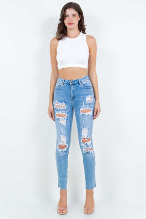 Woman wearing high waist destroyed jeans with a white crop top, showcasing trendy distressed detailing and flattering fit.