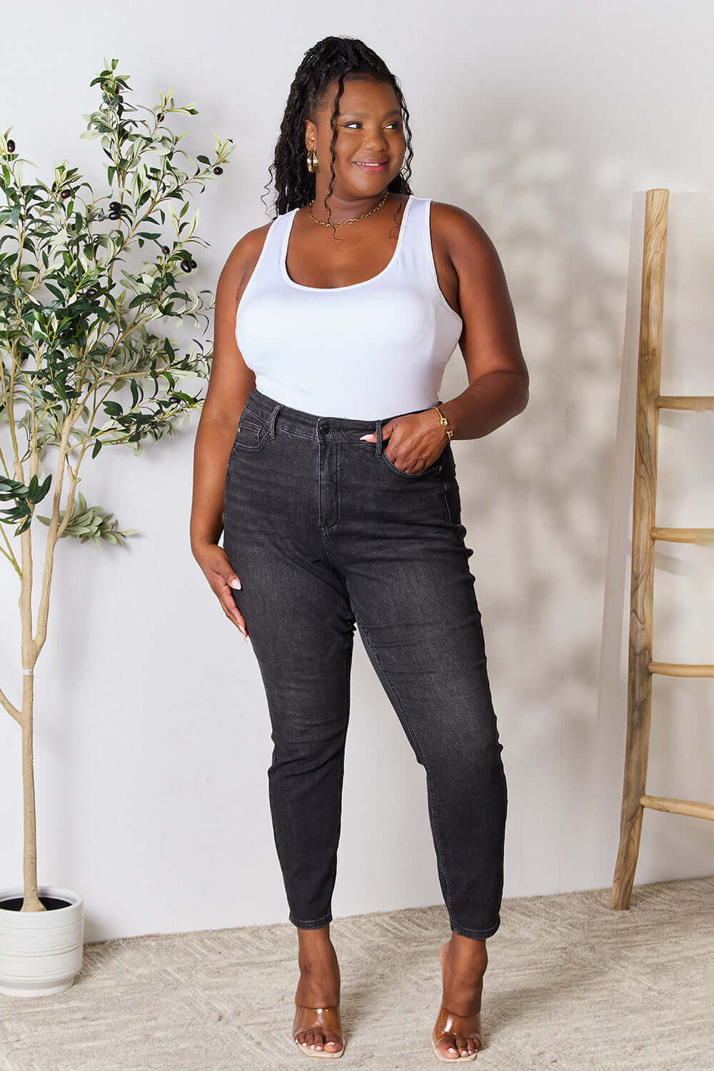 Woman wearing tummy control high waist denim jeans by Judy Blue Jeans, showcasing a slim silhouette with a white tank top.