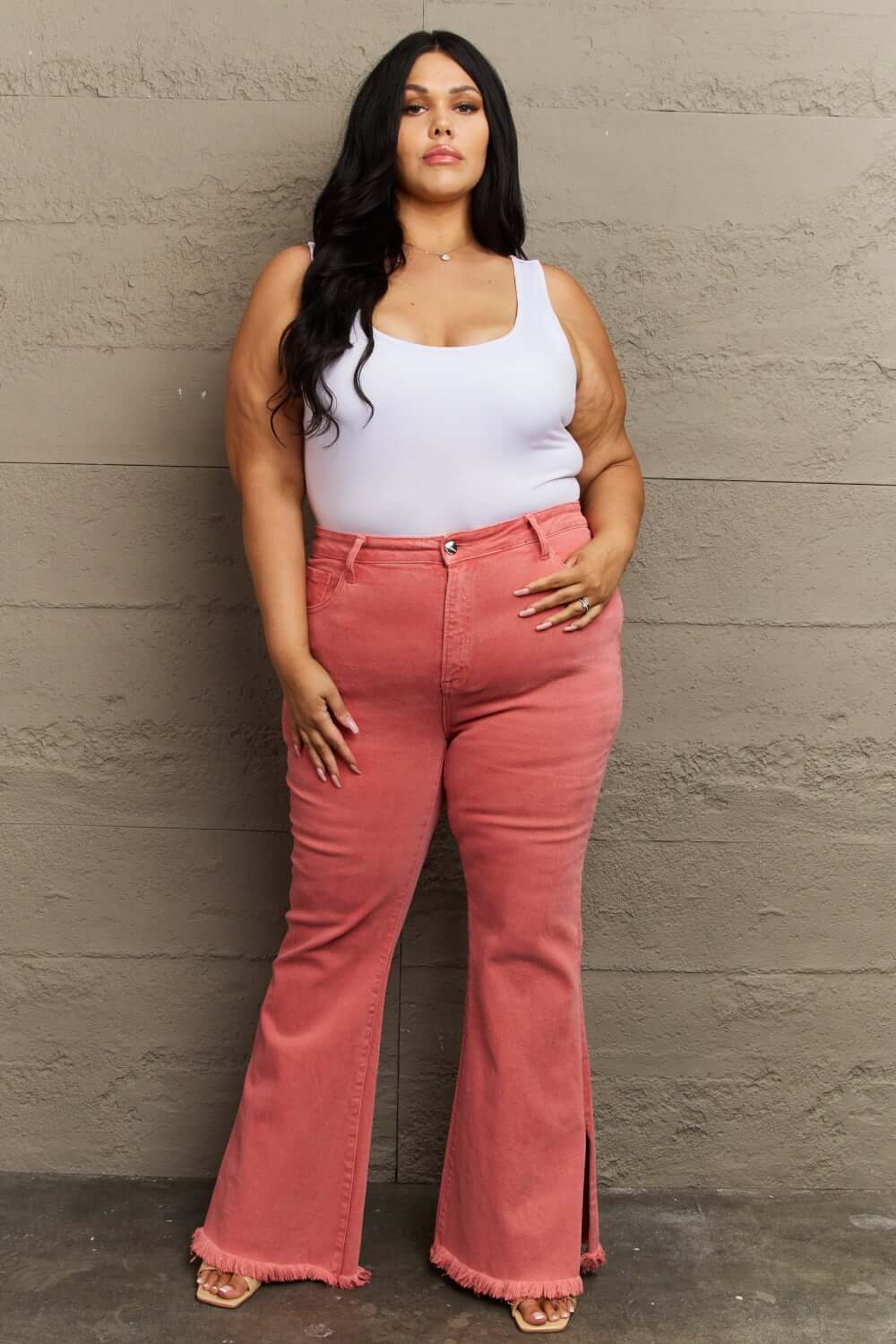 Curvy woman wearing Bailey High Waist Side Slit Flare Jeans in pink, paired with a white tank top, showcasing Risen Jeans' flattering fit.