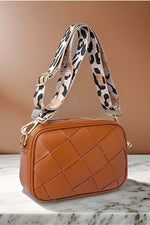 Stylish brown cassette woven crossbody bag with a chic leopard print strap on a marble surface.