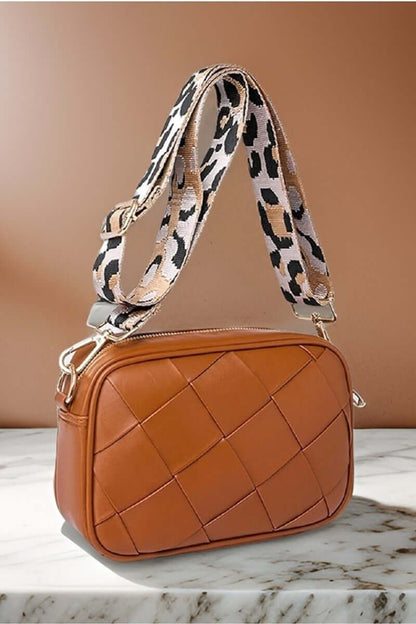 Stylish brown cassette woven crossbody bag with a chic leopard print strap on a marble surface.