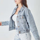 Woman wearing RISEN Full Size Button Down Cropped Denim Jacket with a white top and distressed denim shorts.