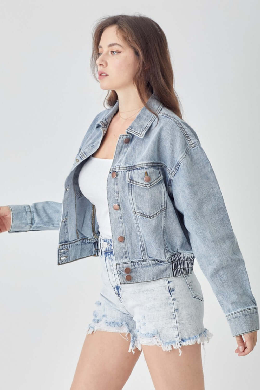 Woman wearing RISEN Full Size Button Down Cropped Denim Jacket with a white top and distressed denim shorts.