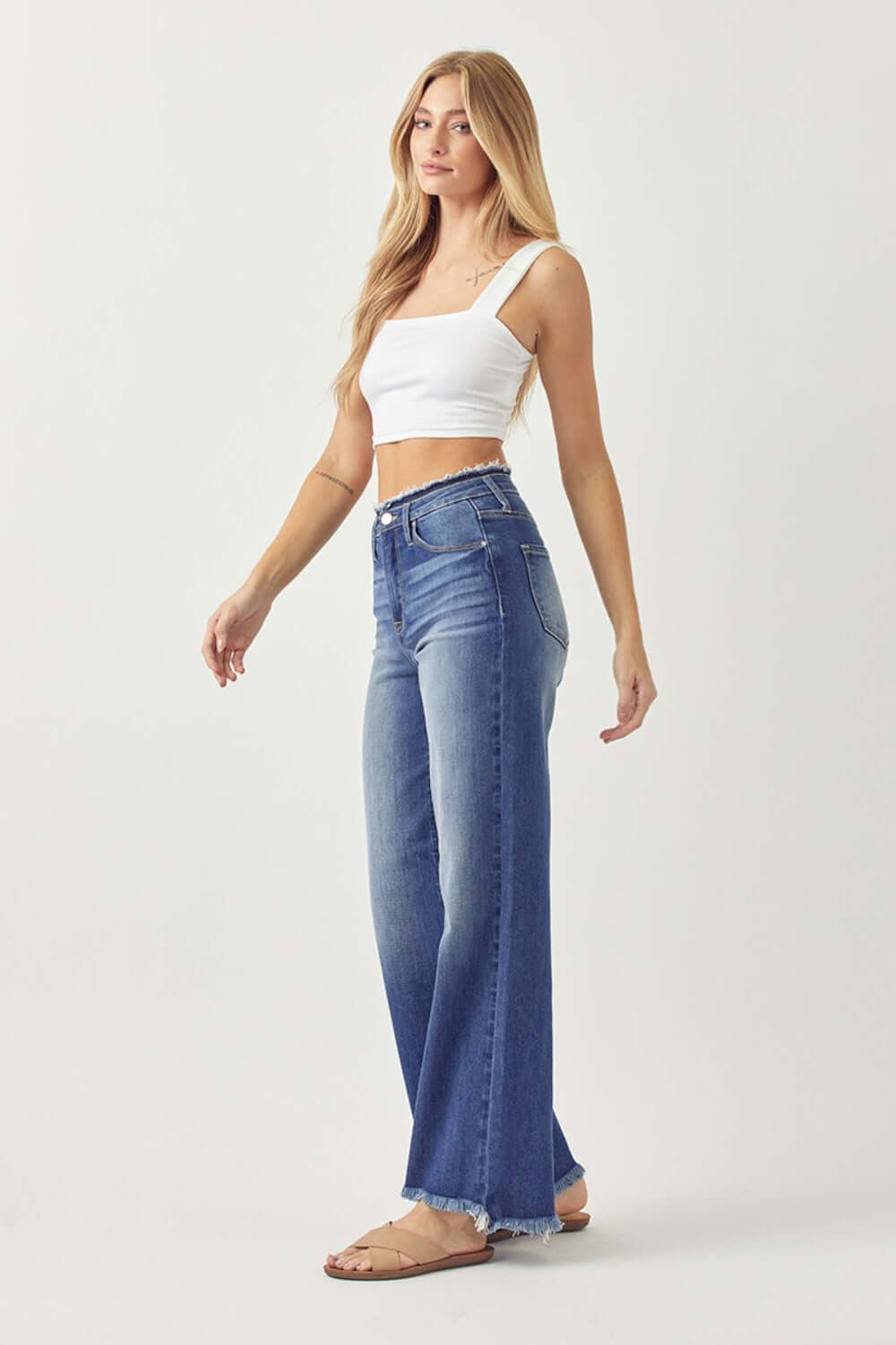 Trendy high waist raw hem wide leg jeans from Risen Jeans, perfect for a chic day-to-night look, modeled with a white crop top.