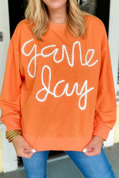 Woman wearing Bella Road Game Day Round Neck Long Sleeve Sweatshirt in orange with "Game Day" text