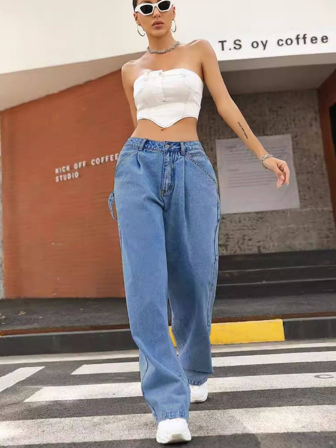 Fashionable woman in wide leg jeans with pockets and white corset top, standing outside.