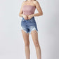 Woman wearing raw hem asymmetrical waist denim shorts by Risen Jeans with a pink strapless top and black ankle boots