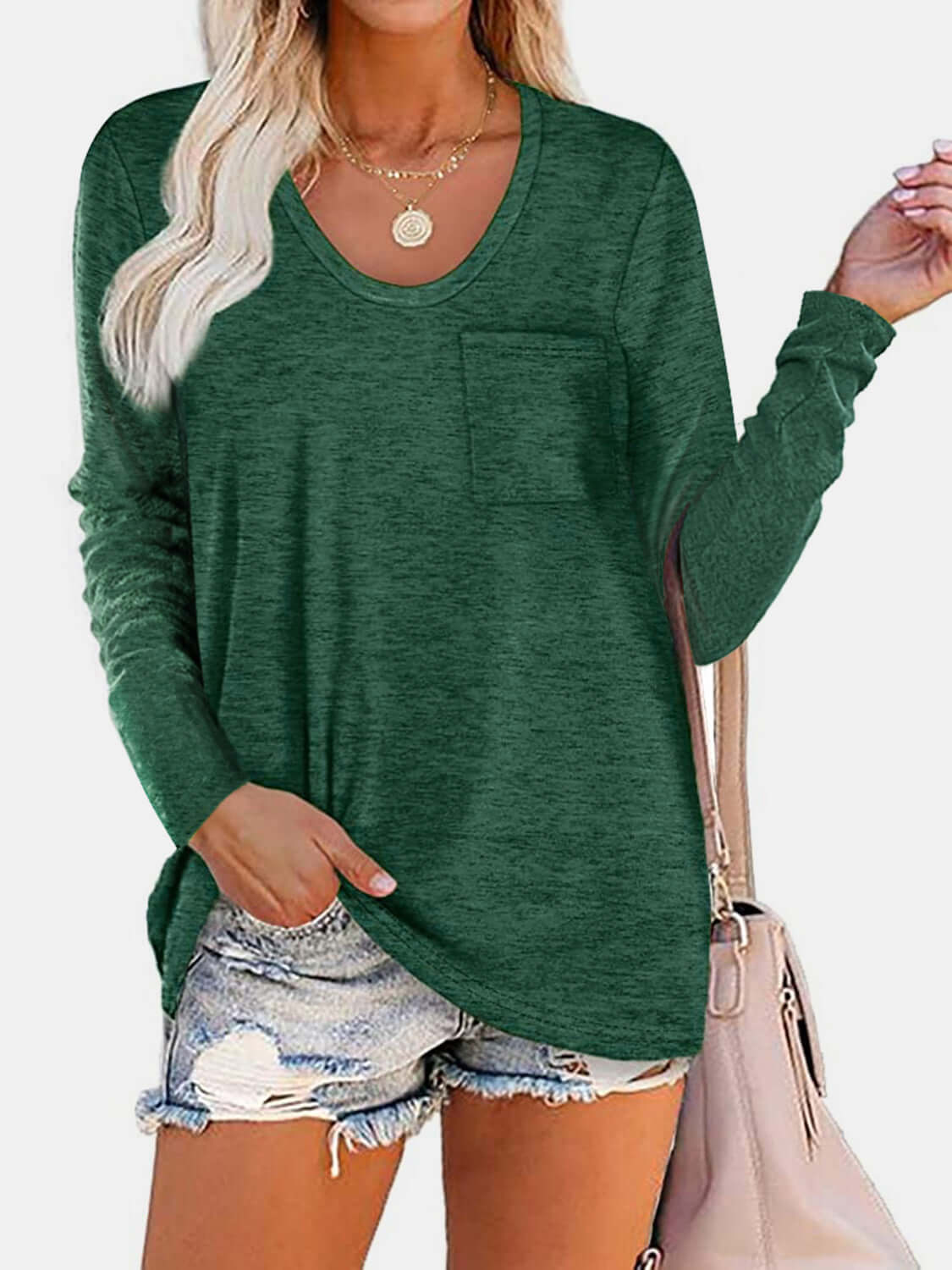 Woman wearing Bella Road round neck long sleeve green T-shirt with a pocket, paired with denim shorts and a beige handbag.