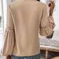 Woman wearing Perfee Frill Tie Neck Long Sleeve Blouse with lace details on sleeves, standing in chic indoor setting