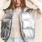 Woman wearing J.NNA shiny metallic puffer vest with snap and zipper closures, paired with a cozy sweater.