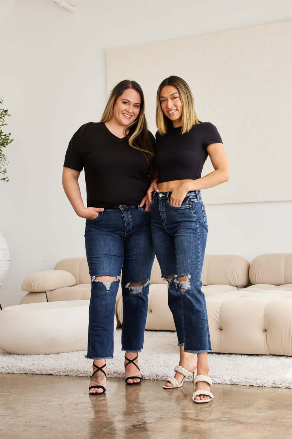 Models wearing RFM Tummy Control Distressed High Waist Raw Hem Jeans in a living room setting