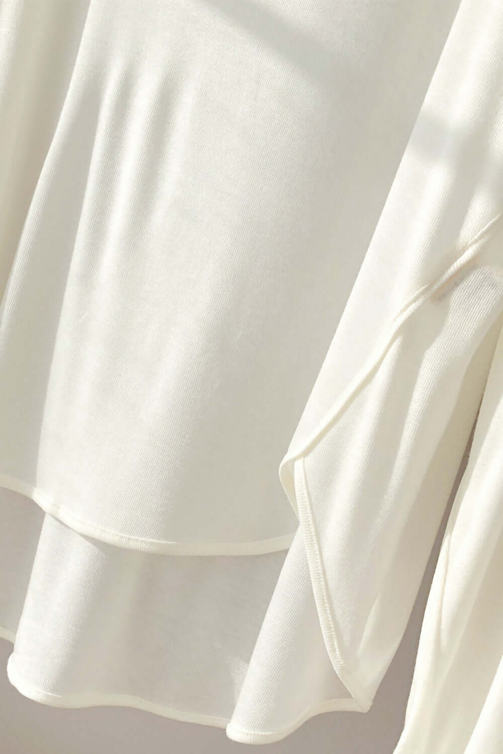 "Close-up of a white high-low long sleeve t-shirt, featuring sheer fabric, slightly stretchy fit, and basic bae chic style."