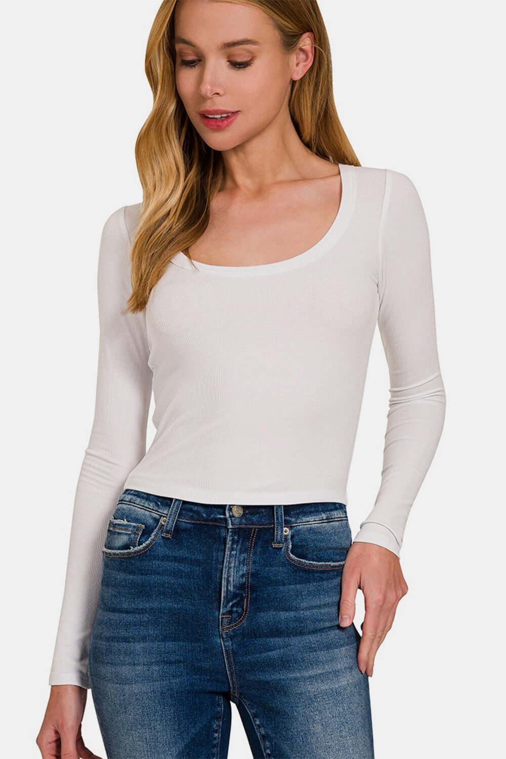 Woman wearing a white scoop neck long sleeve t-shirt paired with blue jeans.