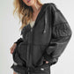 Trendy woman in a black exposed seam zip-up drawstring hooded jacket, styled with denim shorts for a chic look.