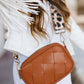 Stylish woman in a white jacket holding a woven tan crossbody bag with leopard strap, showcasing fashion and functionality.